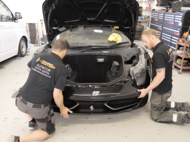 Technicians refitting the front bumper of a black Ferrari