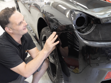 Technician checking panel alignment by the rear wheel arch of a Ferrari