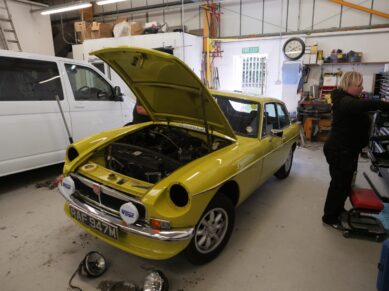 Yellow classic MGB GT in the workshop with the bonnet up